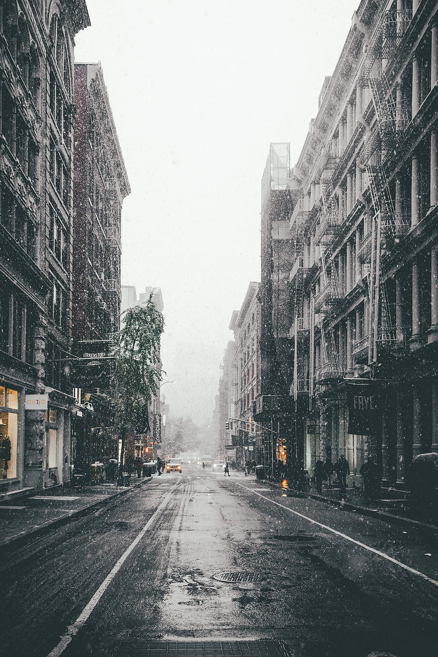 Moody Urban Street Scene During Snowfall with Wet Pavement and Historic Architecture HD phone wallpaper