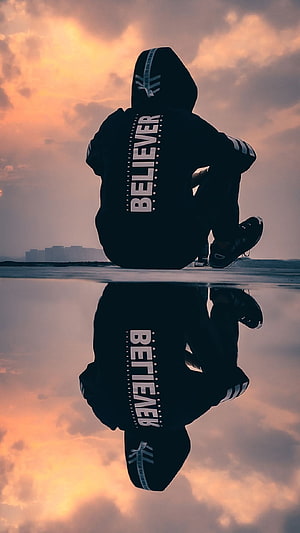 Silhouette of a Hooded Figure Sitting by a Reflective Water Surface at Sunset HD phone wallpaper