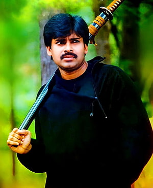 Pawan Kalyan in a black jacket holding a katana sword in a lush green forest setting HD phone wallpaper