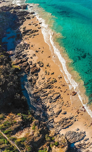 Aerial View of Turquoise Coastline with Rocky Beach and Gentle Waves HD phone wallpaper
