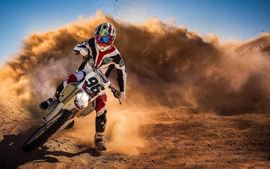 Motocross Rider Cornering Through Dust Cloud on Dirt Track HD wallpaper