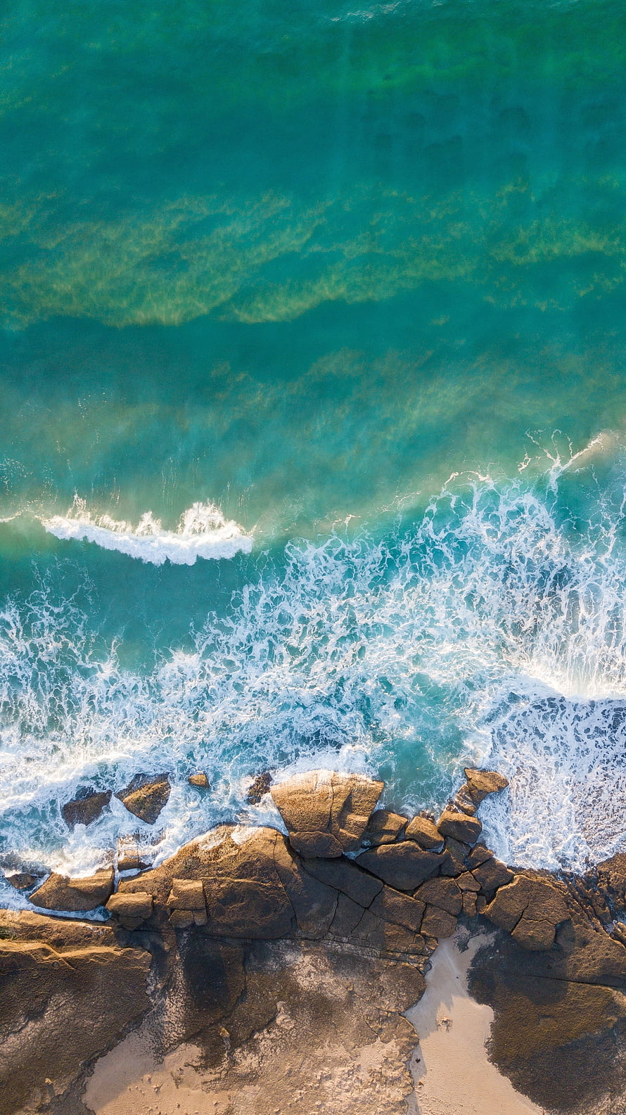Aerial View of Turquoise Ocean Waves Crashing Against Rugged Coastal Rocks HD phone wallpaper