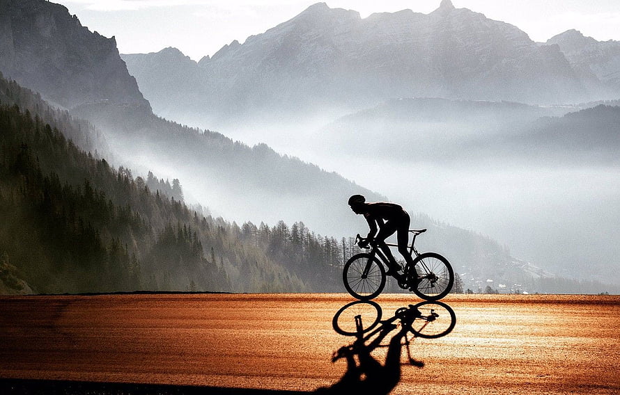 Silhouette of a cyclist riding through a misty mountain valley at sunrise HD wallpaper