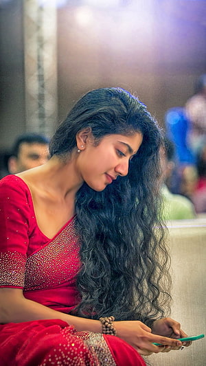 Sai Pallavi in a red embroidered saree looking at a smartphone HD phone wallpaper