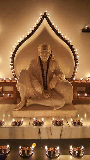 Sai Baba Statue in Serene Meditation Pose Surrounded by Warm Oil Lamps and Candlelight HD phone wallpaper