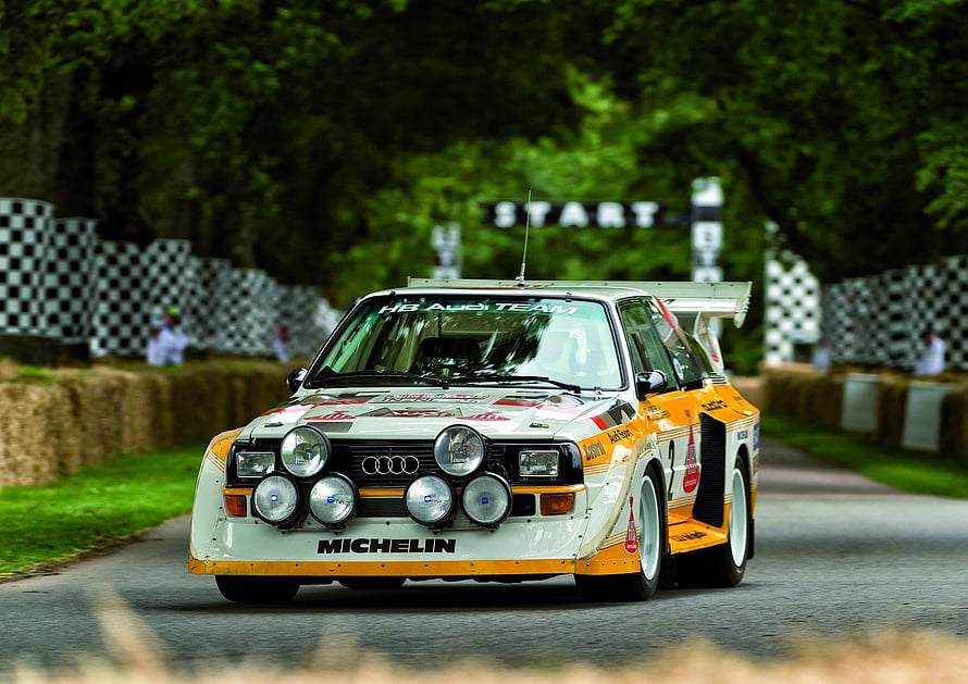 Audi Sport Quattro S1 rally car crossing the start line at a classic motorsport event HD wallpaper