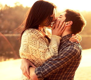 Romantic couple sharing a tender kiss in warm golden hour sunlight HD wallpaper
