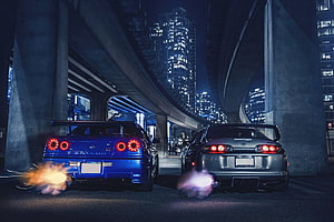 Nissan Skyline GT-R R34 and Toyota Supra drifting side by side under a city overpass at night HD wallpaper