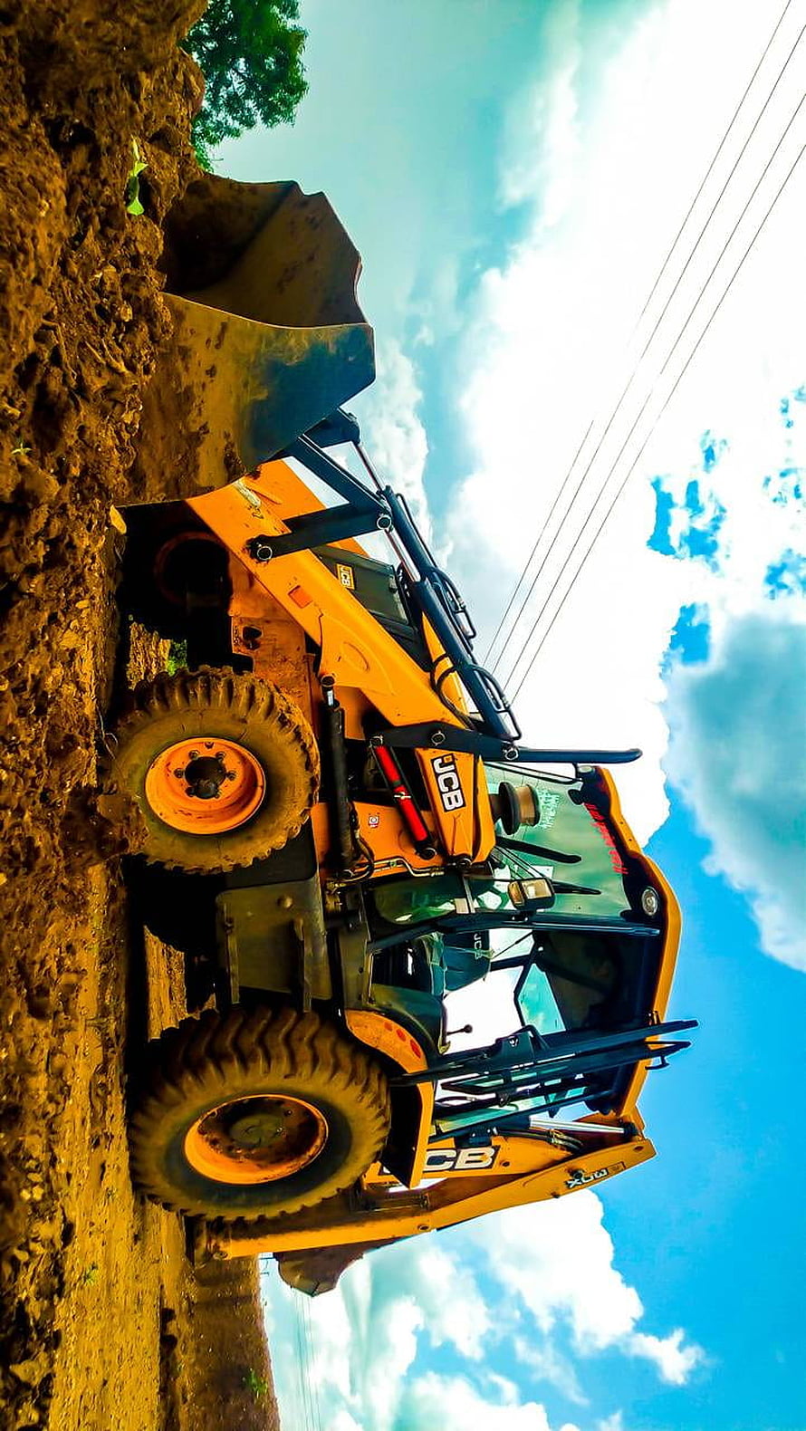 JCB Backhoe Loader Digging in Muddy Construction Site Under Blue Sky HD phone wallpaper
