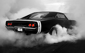 Black Dodge Charger R/T performing a burnout with thick tire smoke on an asphalt track HD wallpaper