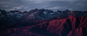 Dramatic Red Mountain Range at Dusk with Snow-Capped Peaks and Moody Sky HD wallpaper