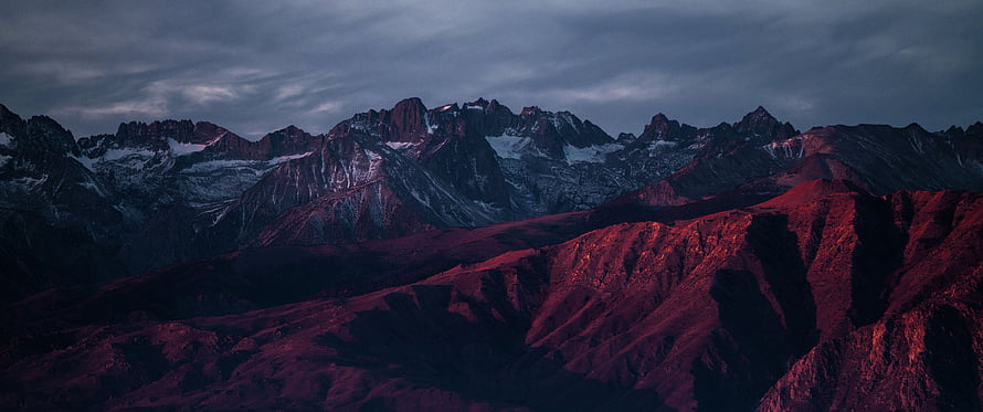 Dramatic Red Mountain Range at Dusk with Snow-Capped Peaks and Moody Sky HD wallpaper