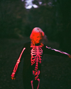 Phoebe Bridgers in a glowing skeleton bodysuit under red light in a dark forest HD phone wallpaper