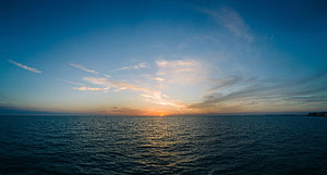 Golden sunset over a calm ocean horizon with wispy clouds and deep blue sky HD wallpaper