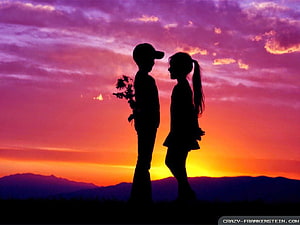 Silhouetted couple holding flowers against a vibrant sunset sky with distant mountains HD wallpaper