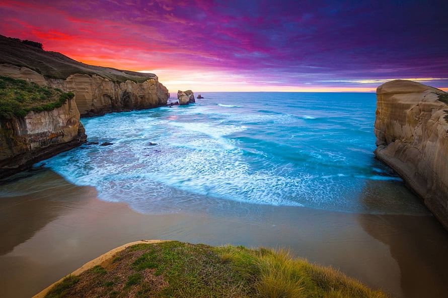 Vibrant sunset over a secluded cove with dramatic limestone cliffs and turquoise ocean waves HD wallpaper