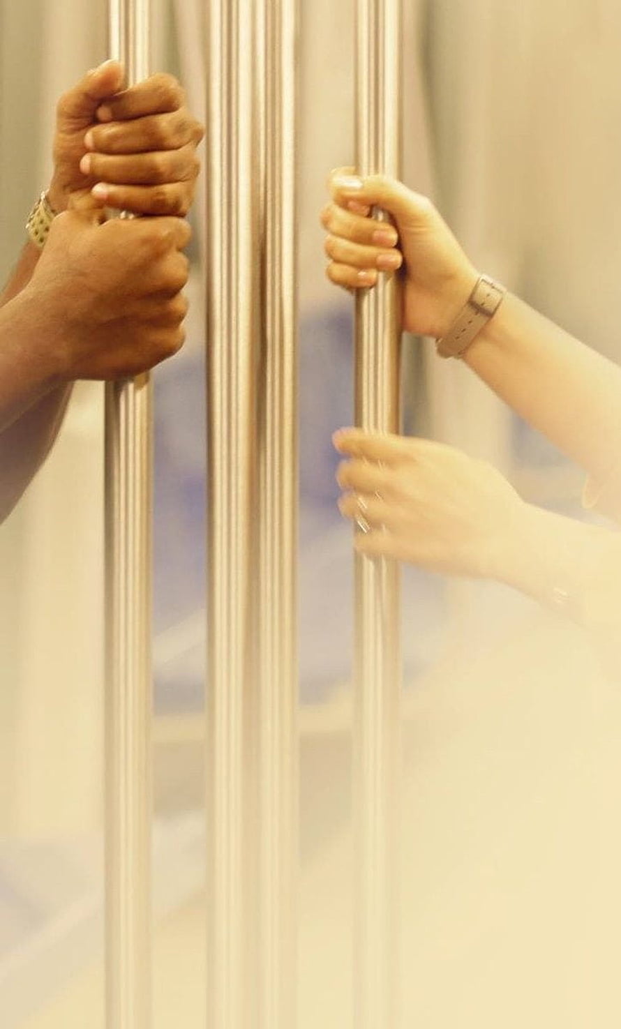 Two Pairs of Hands Gripping Vertical Metal Bars in Soft Warm Light HD phone wallpaper