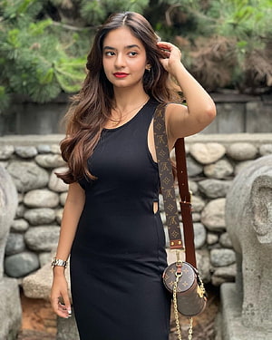 Anushka Sen in a black sleeveless dress with a Louis Vuitton bag against a stone wall HD phone wallpaper