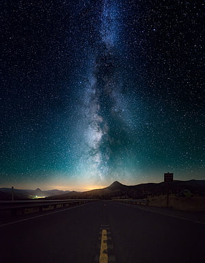 Milky Way Galaxy Arching Over a Desert Highway at Night with Distant Mountain Silhouettes HD phone wallpaper