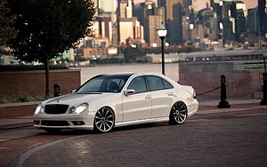White Mercedes-Benz W211 E-Class Sedan Parked on Brick Promenade with City Skyline HD wallpaper