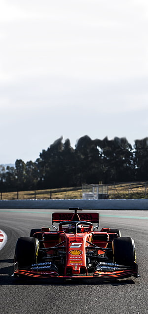Red Ferrari Formula 1 race car speeding on a track with sponsor logos and open sky background HD phone wallpaper