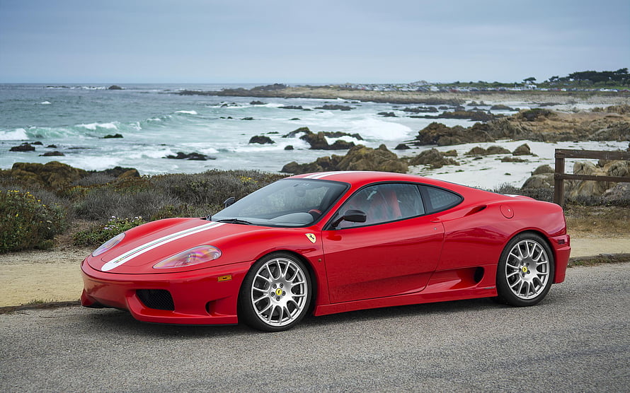 Red Ferrari 360 Modena with white racing stripes parked on a coastal road overlooking the ocean HD wallpaper