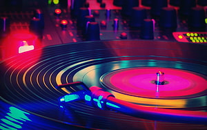 Neon-lit DJ turntable with spinning vinyl record and glowing mixer controls in a vibrant club setting HD wallpaper