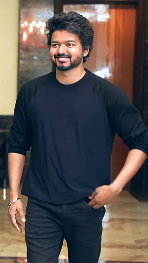 Vijay in a black long-sleeve shirt and dark trousers, smiling in an indoor setting HD phone wallpaper
