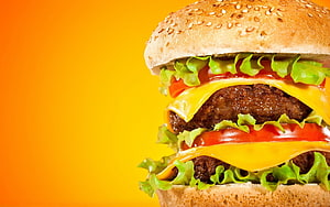 Double Cheeseburger with Sesame Bun, Lettuce, Tomato, and Melted Cheese on a Vibrant Orange Background HD wallpaper
