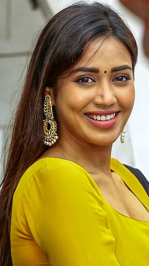 Nivetha Thomas in a bright yellow top with ornate gold jhumka earrings and a warm smile HD phone wallpaper