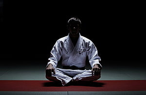 Judo practitioner in white gi meditating in seiza position on a dark dojo mat HD wallpaper