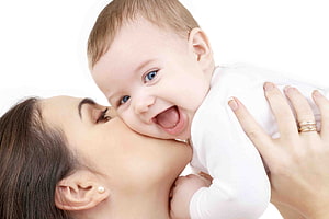 Mother Kissing Her Smiling Baby On The Cheek In A Bright Studio Setting HD wallpaper