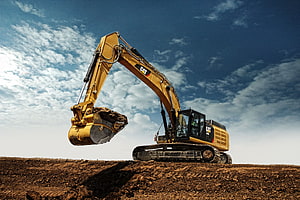 Caterpillar Excavator Lifting Soil on a Construction Site Under a Blue Sky HD wallpaper