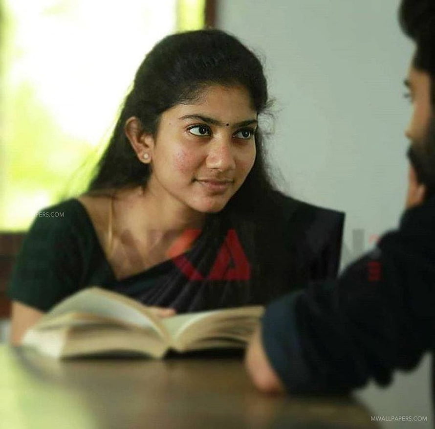 Sai Pallavi in a black sari with red accents, seated at a table with an open book HD wallpaper