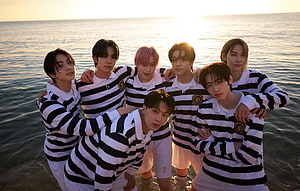 Enhypen members in striped polo shirts posing together at the ocean during golden hour HD wallpaper