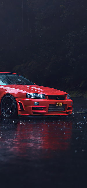 Red Nissan Skyline GT-R R34 parked on wet asphalt in the rain with dark forest background HD phone wallpaper