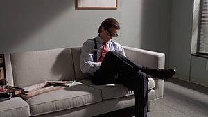 Patrick Bateman from American Psycho relaxing on a beige couch in a minimalist office HD wallpaper