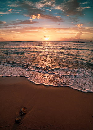 Golden sunset over a calm ocean with gentle waves lapping onto a sandy beach at dusk HD phone wallpaper
