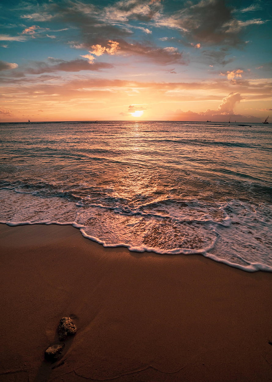 Golden sunset over a calm ocean with gentle waves lapping onto a sandy beach at dusk HD phone wallpaper