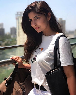Kashmira Pardeshi in a white graphic t-shirt and white pants with a black tote bag on a city balcony HD phone wallpaper