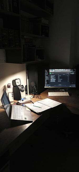 Dimly lit home office desk with laptop, monitor, and notebook for late night study HD phone wallpaper
