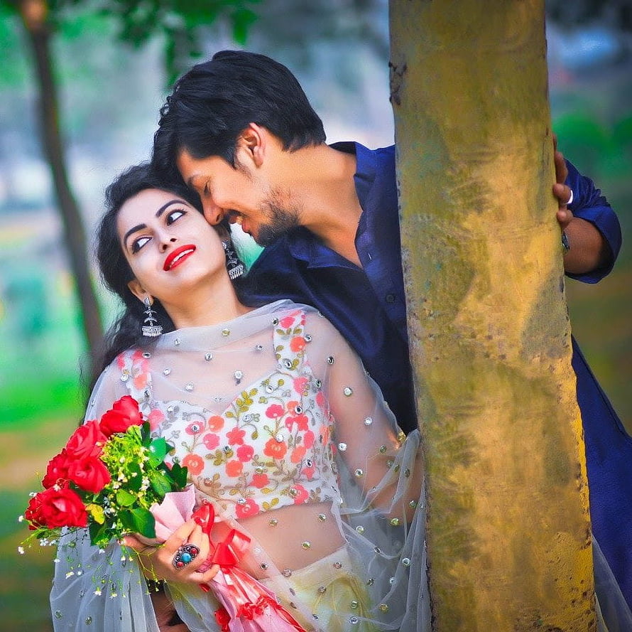 Romantic Indian couple in traditional attire holding red roses by a tree HD wallpaper