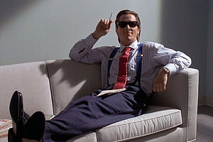 Patrick Bateman in American Psycho wearing sunglasses and a red tie while lounging on a sofa, Patrick Bateman's Rolex Datejust heralded the new 'executive style'. British GQ HD wallpaper