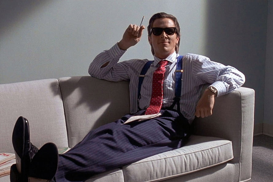 Patrick Bateman in American Psycho wearing sunglasses and a red tie while lounging on a sofa, Patrick Bateman's Rolex Datejust heralded the new 'executive style'. British GQ HD wallpaper
