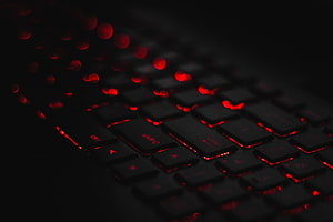 Close-up of a black mechanical keyboard with red backlighting and bokeh effect in a dark setting HD wallpaper