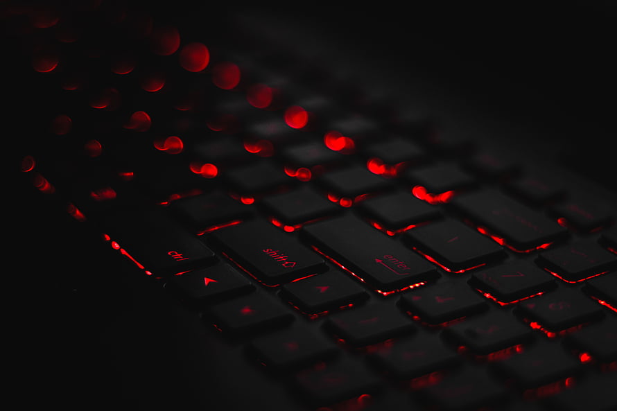 Close-up of a black mechanical keyboard with red backlighting and bokeh effect in a dark setting HD wallpaper