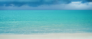 Serene Turquoise Ocean Water Lapping Against White Sand Beach Under Dramatic Clouds HD wallpaper