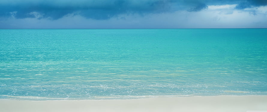 Serene Turquoise Ocean Water Lapping Against White Sand Beach Under Dramatic Clouds HD wallpaper