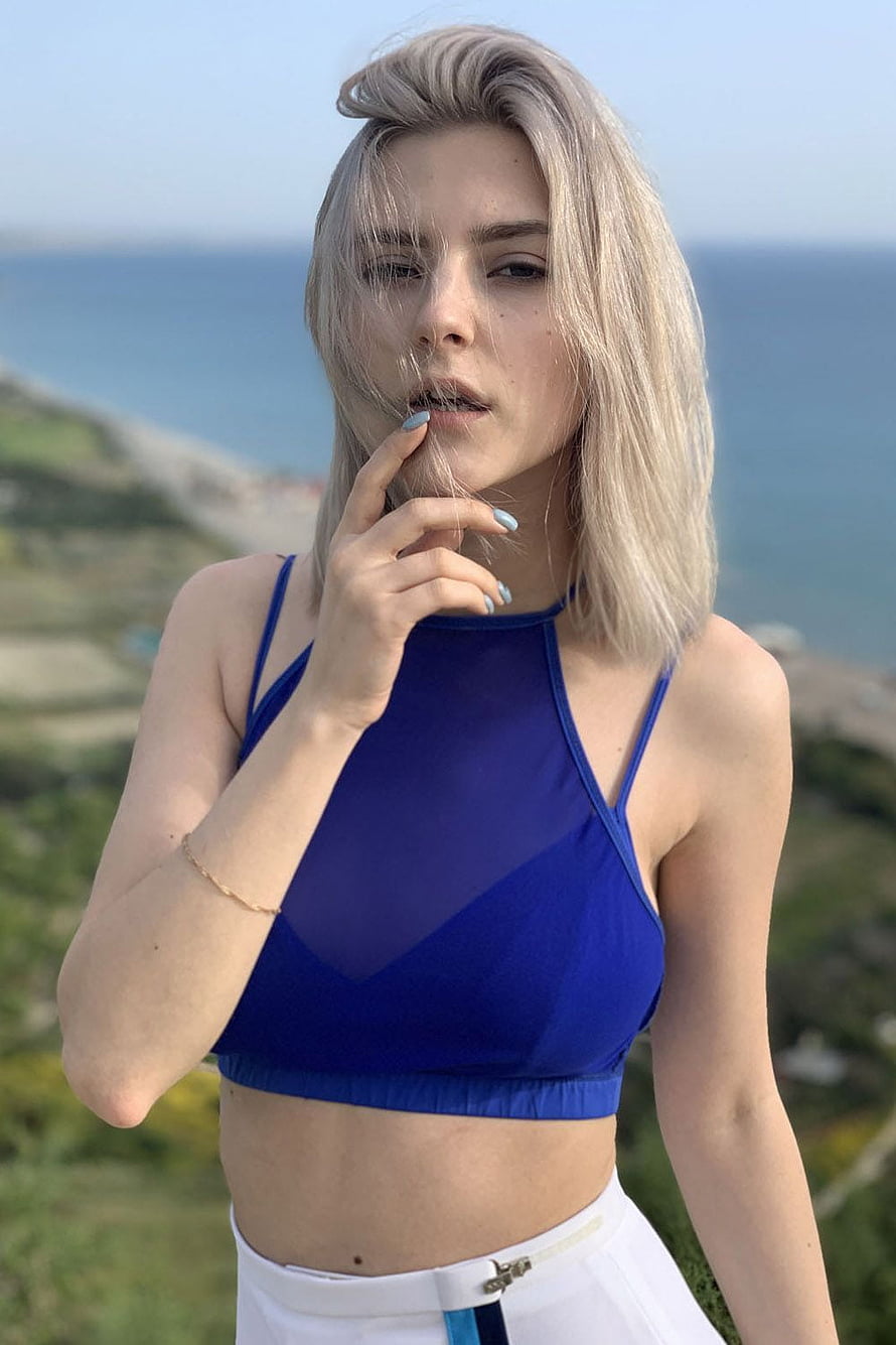 Eva Elfie in a blue crop top and white pants against a coastal cliff backdrop HD phone wallpaper