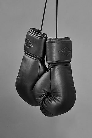 Black Leather Boxing Gloves Hanging on Cords Against a Gray Studio Background HD phone wallpaper